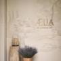 Entrance to Aelia Spa at Auberge Collection, featuring a hand-painted wall mural with the spa logo, a rustic wooden pedestal, and a pot of lavender in warm, natural light.