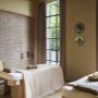 Serene treatment room at Aelia Spa with soft beige tones, natural wood furnishings, and floor-to-ceiling windows letting in garden light.